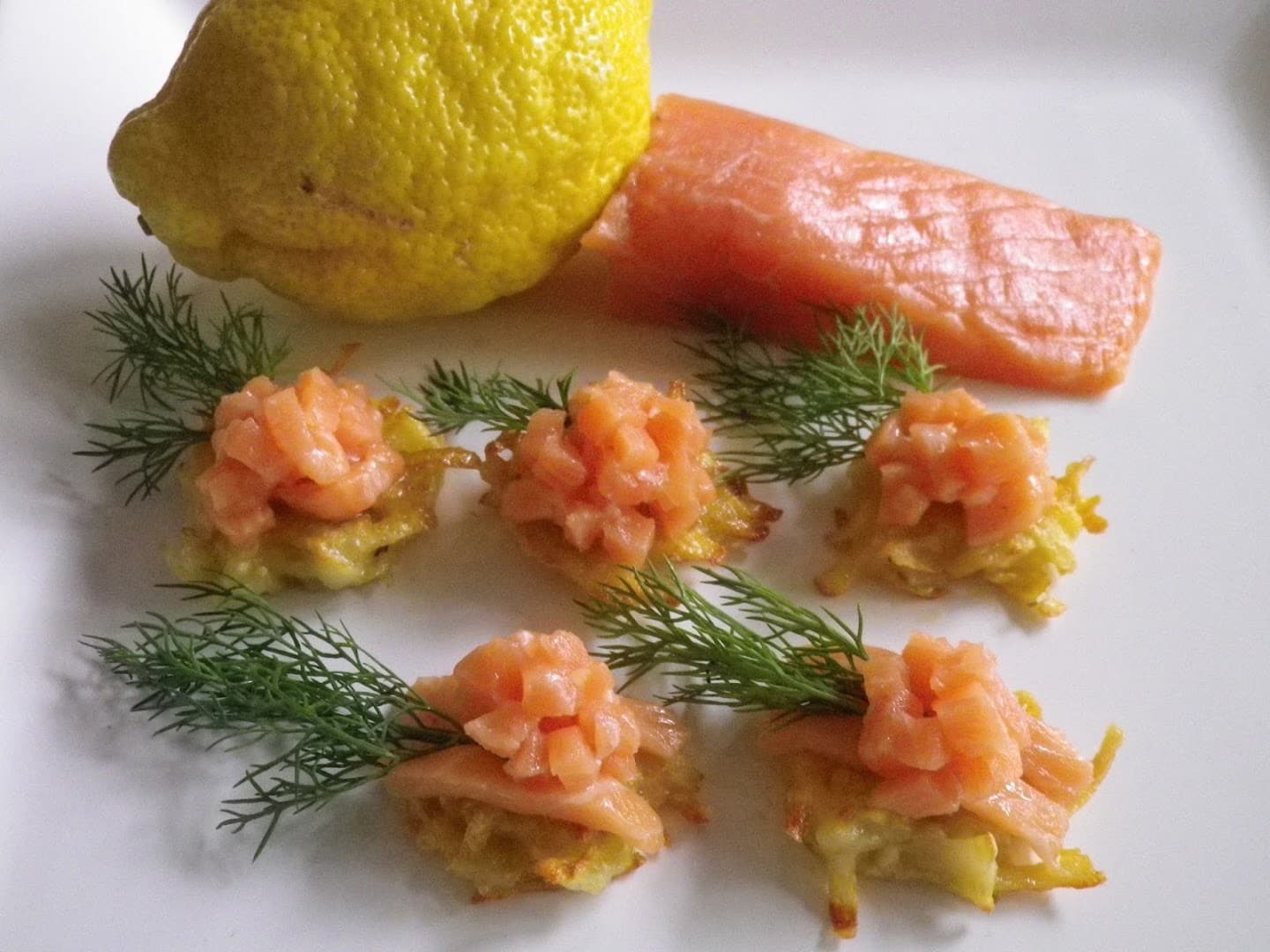 Lachstatar auf Rösti mit Dill, dahinter eine Zitrone und ein Stück Lachsfilet