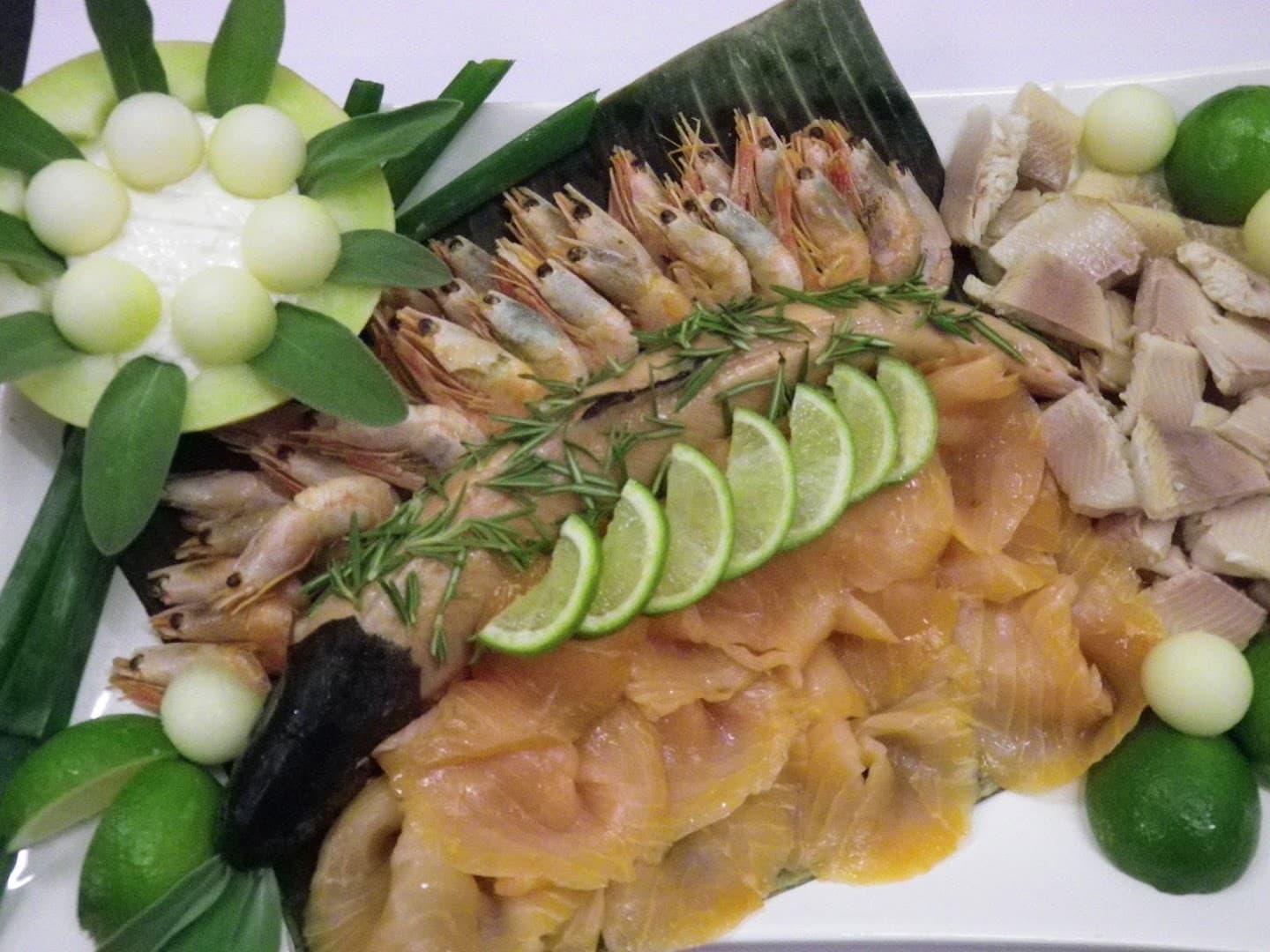 Platte mit Garnelen, Räucherlachs, Forelle, Limettenspalten und Melonenkugeln