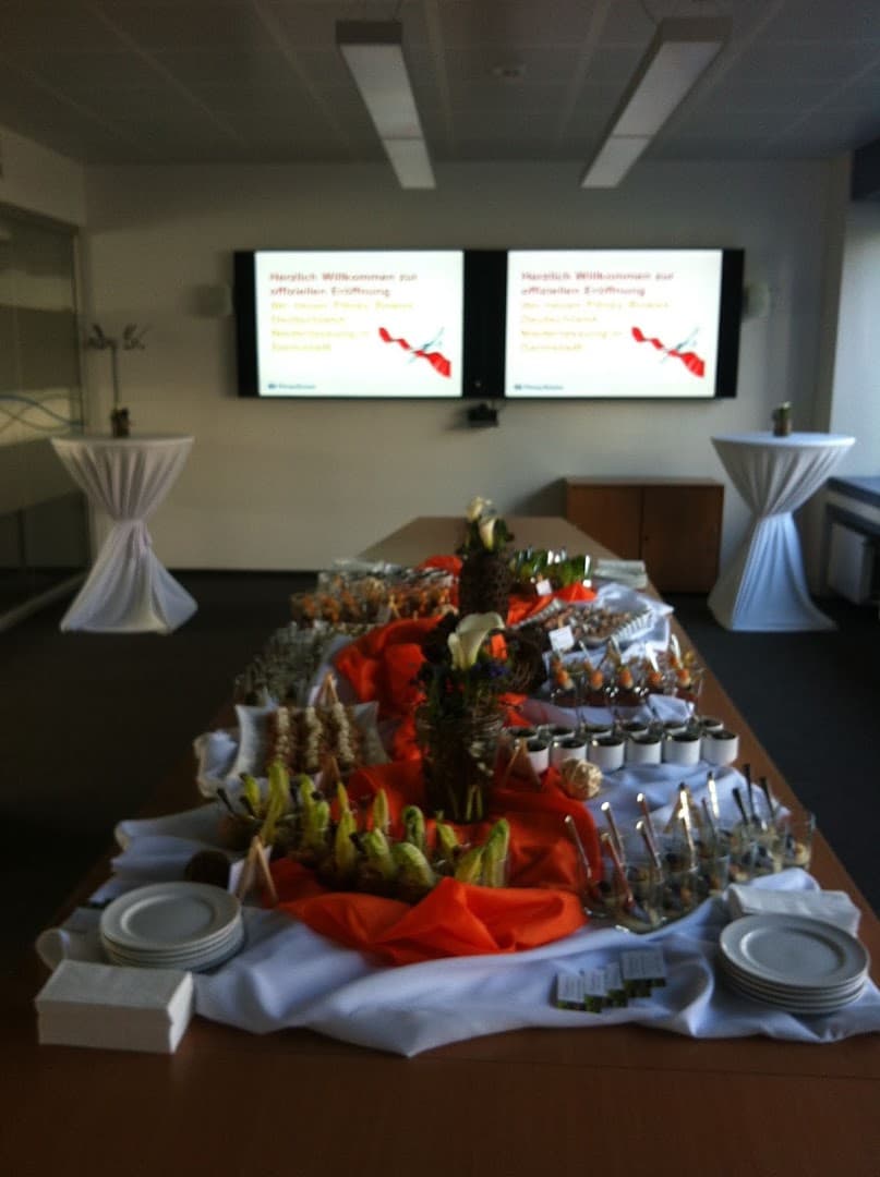 Lange Buffettafel mit orangefarbenen Tüchern, Calla, Gläsern und Tellerstapeln in einem Veranstaltungsraum
